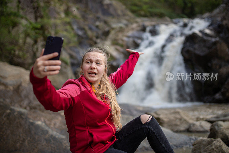 年轻的徒步旅行者在大自然中用她的智能手机为她的粉丝打视频电话/录制视频